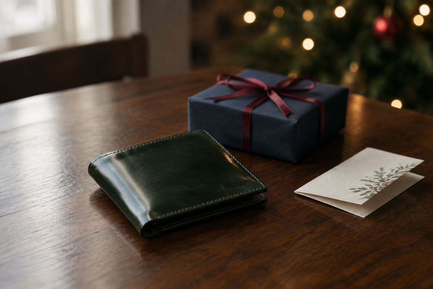 クリスマスのギフトボックスと並べた深緑のコードバンの二つ折り財布